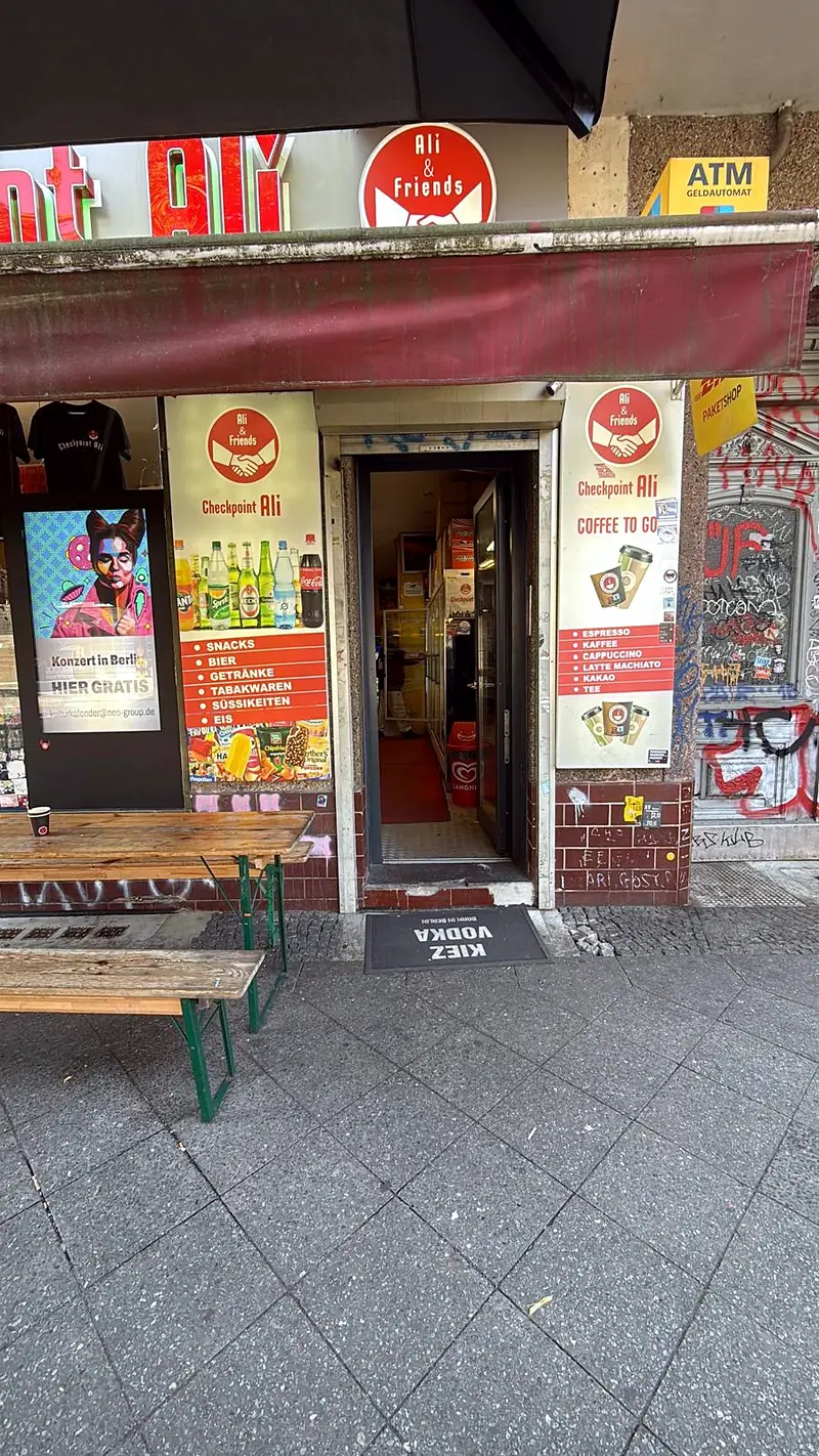 Eingang von Checkpoint Ali an der Wiener Straße 14 mit Coffee-to-go-Aushang und Sitzbank davor